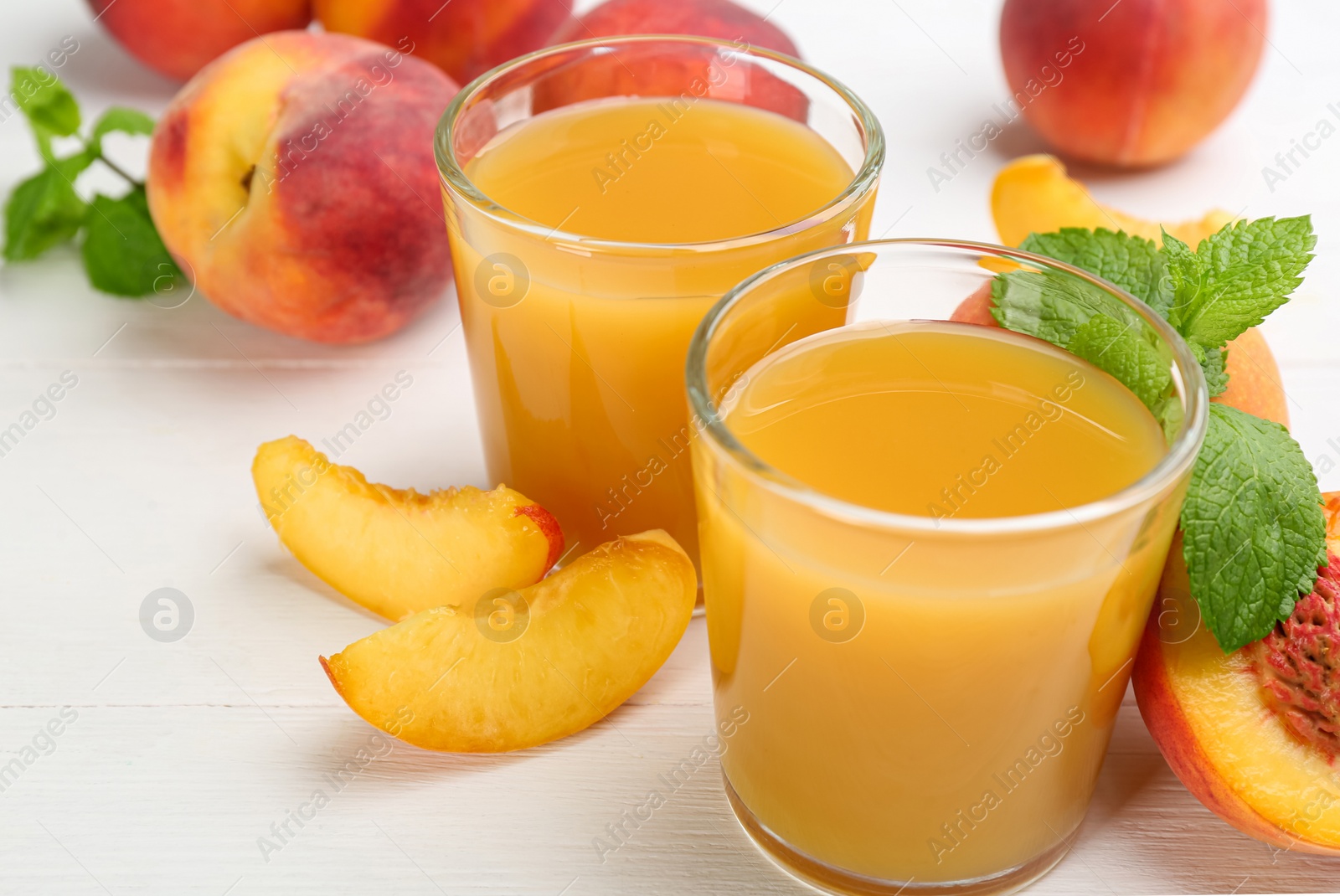 Photo of Natural peach juice and fresh fruits on white wooden table, closeup