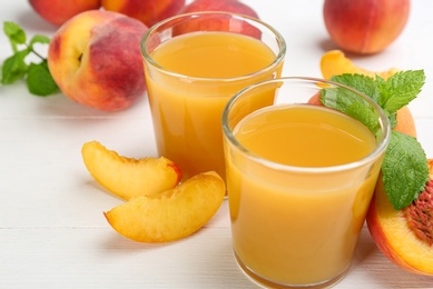 Photo of Natural peach juice and fresh fruits on white wooden table, closeup