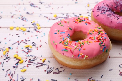 Photo of Glazed donuts decorated with sprinkles on white wooden table, closeup. Space for text. Tasty confectionery