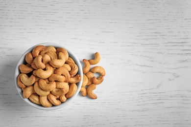 Photo of Tasty cashew nuts in bowl on wooden table, top view. Space for text