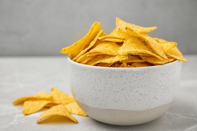 Bowl with tasty Mexican nachos chips on grey table, space for text