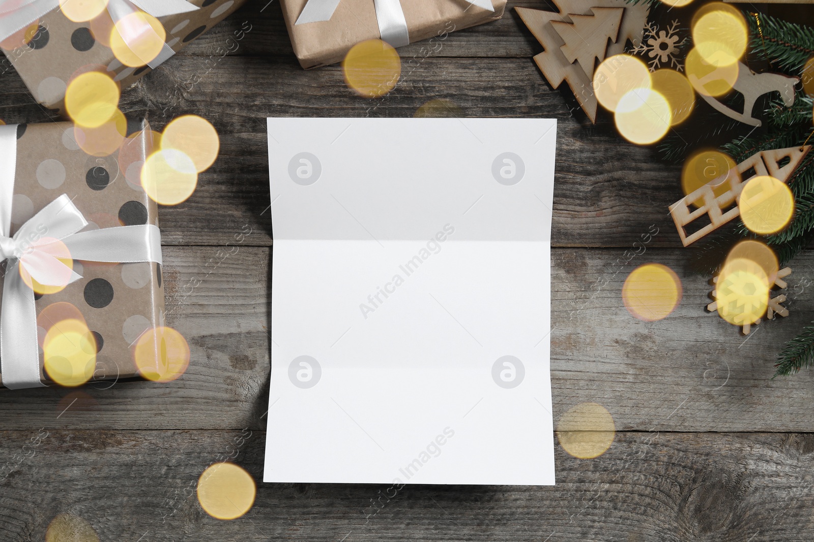 Photo of Flat lay composition with blank paper sheet, gift boxes and Christmas decor on wooden table, space for text. Letter to Santa
