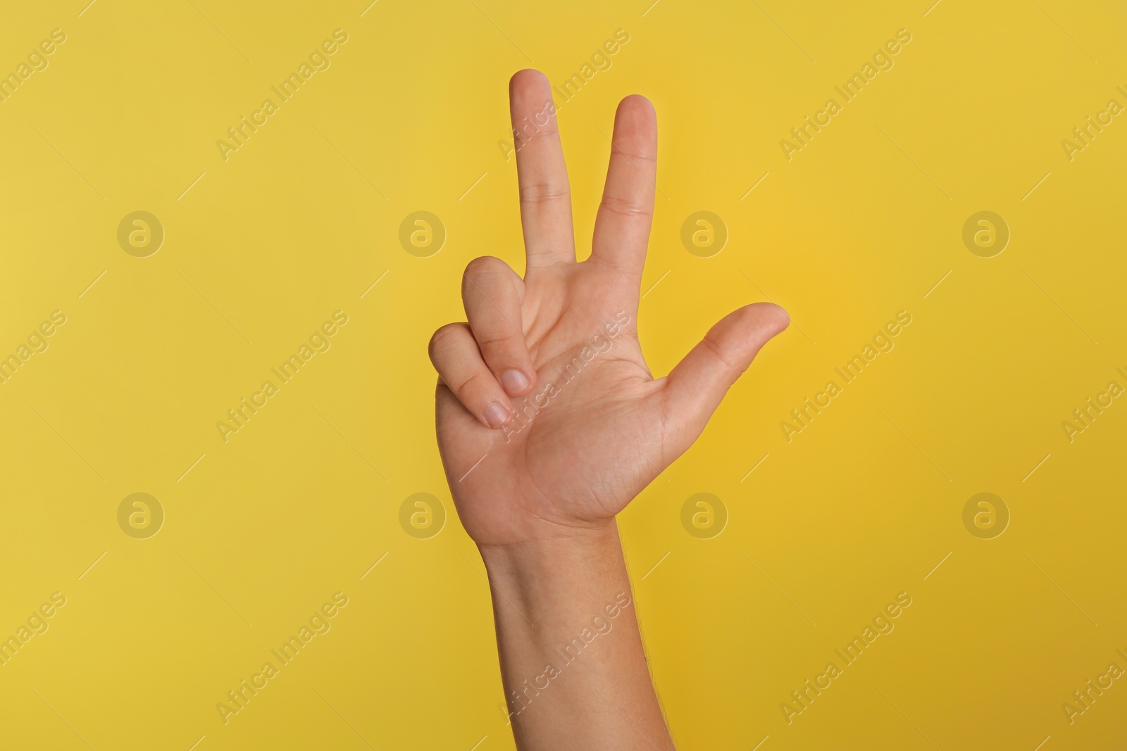 Photo of Teenage boy showing three fingers on yellow background, closeup