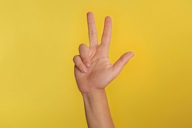 Photo of Teenage boy showing three fingers on yellow background, closeup