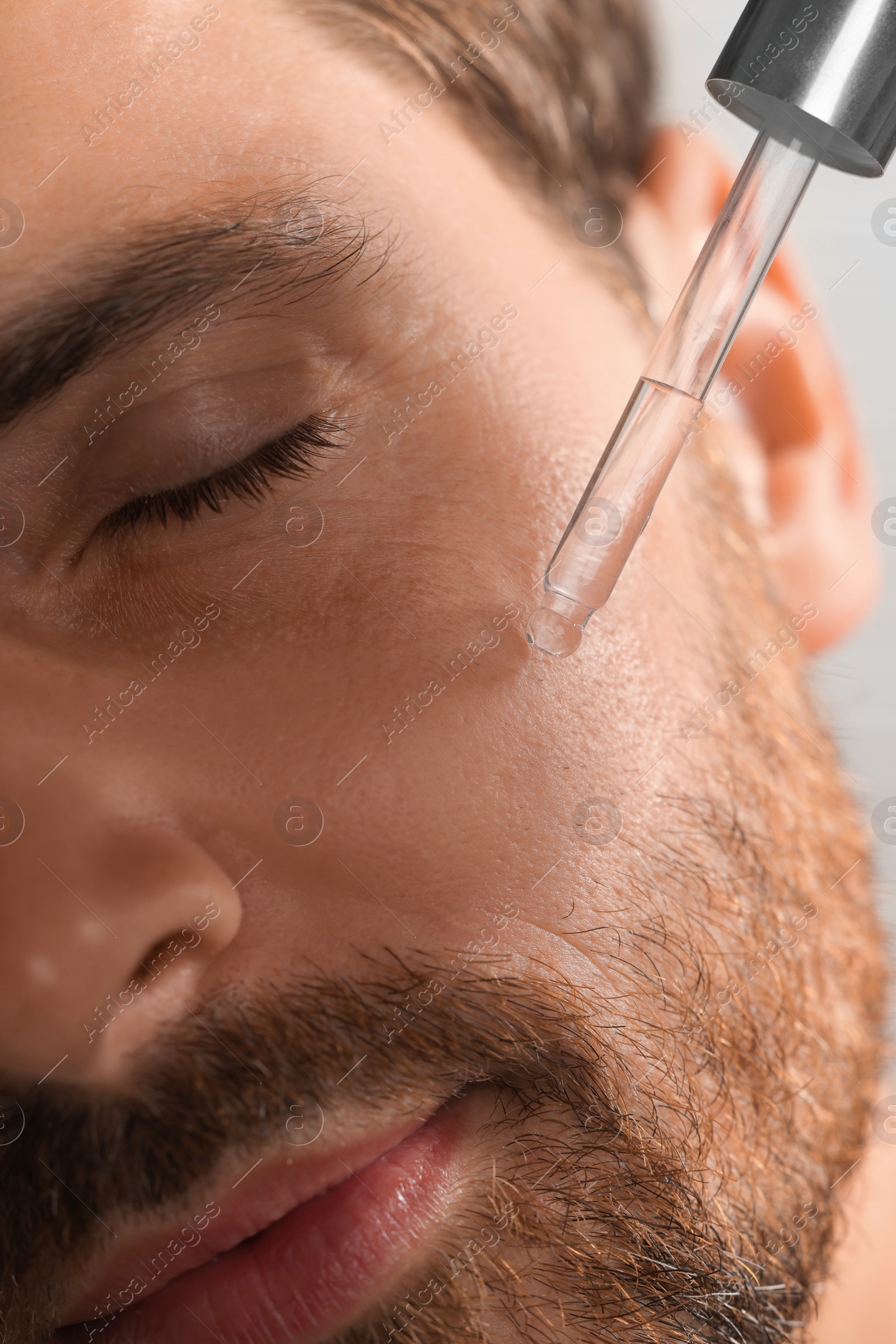 Photo of Handsome man applying cosmetic serum onto his face, closeup