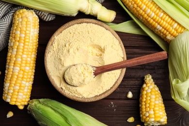 Photo of Corn flour in bowl and fresh cobs on wooden table, flat lay