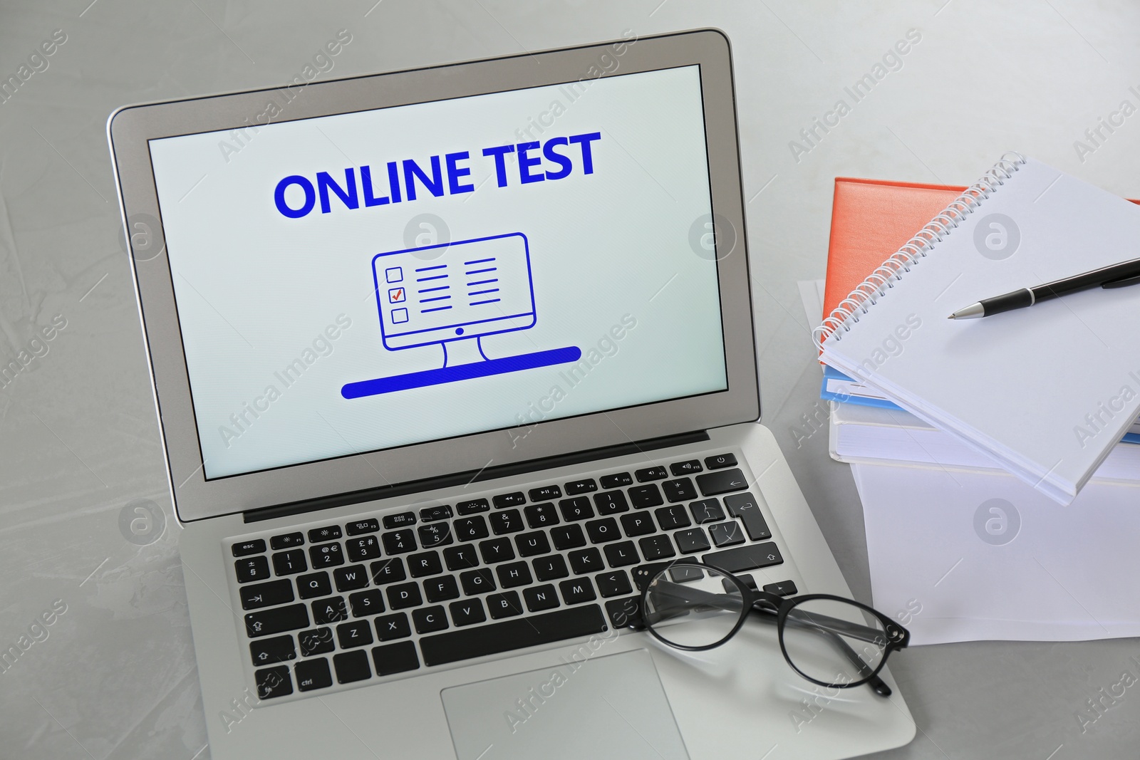 Photo of Laptop with online test, glasses and stationery on grey table