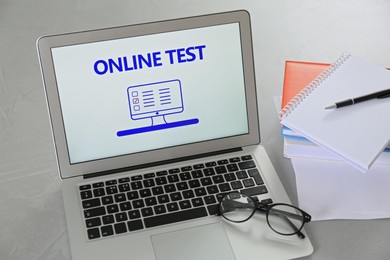 Photo of Laptop with online test, glasses and stationery on grey table