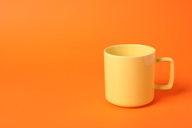 Photo of One yellow ceramic mug on orange background, space for text