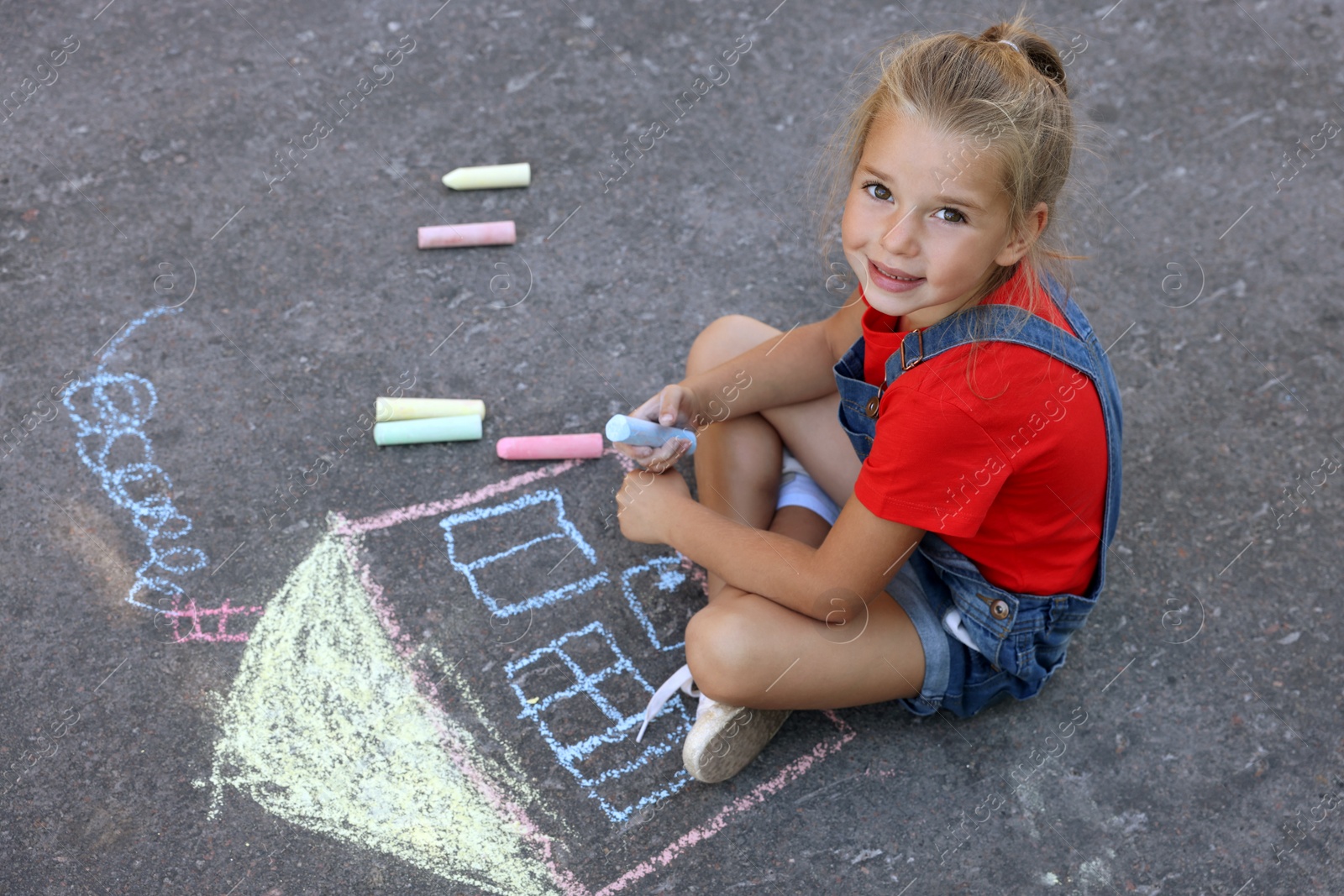 Photo of Cute little child drawing house with colorful chalk on asphalt