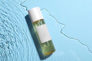 Bottle of cosmetic oil in water on light blue background, top view