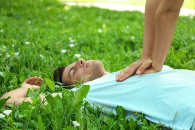 Photo of Young woman performing CPR on unconscious man outdoors, closeup. First aid