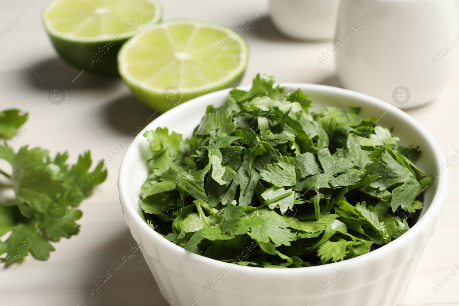 Photo of Cut fresh green cilantro in bowl on white table, closeup