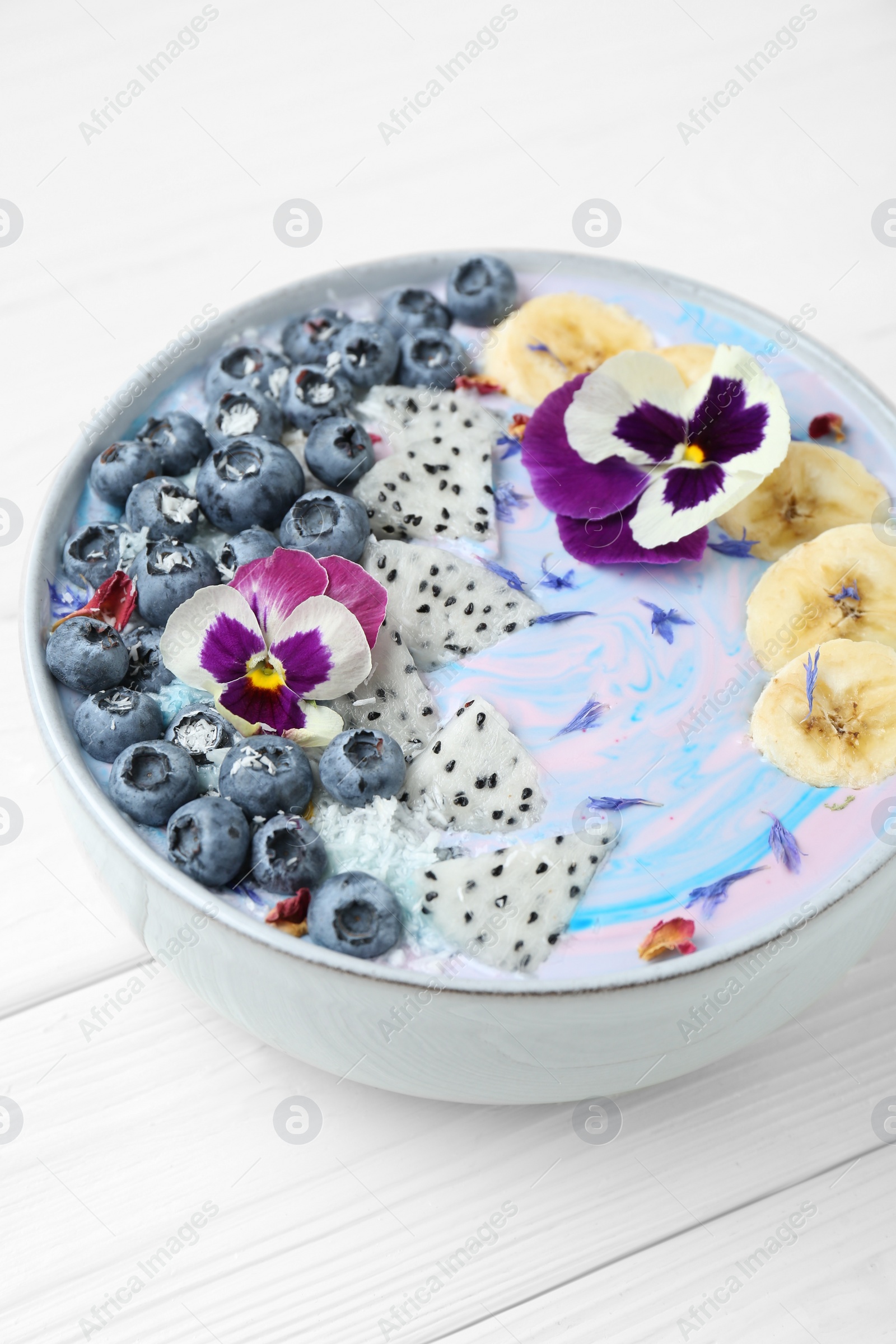 Photo of Delicious smoothie bowl with fresh fruits, blueberries and flowers on white wooden table, closeup