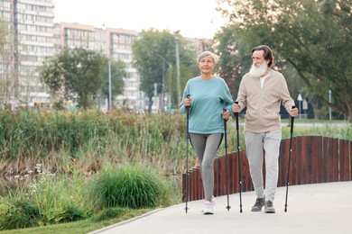 Senior man and woman performing Nordic walking outdoors, space for text