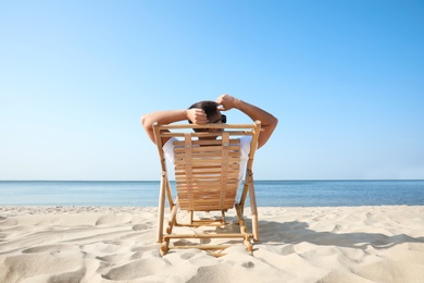 Photo of Young man relaxing in deck chair on sandy beach