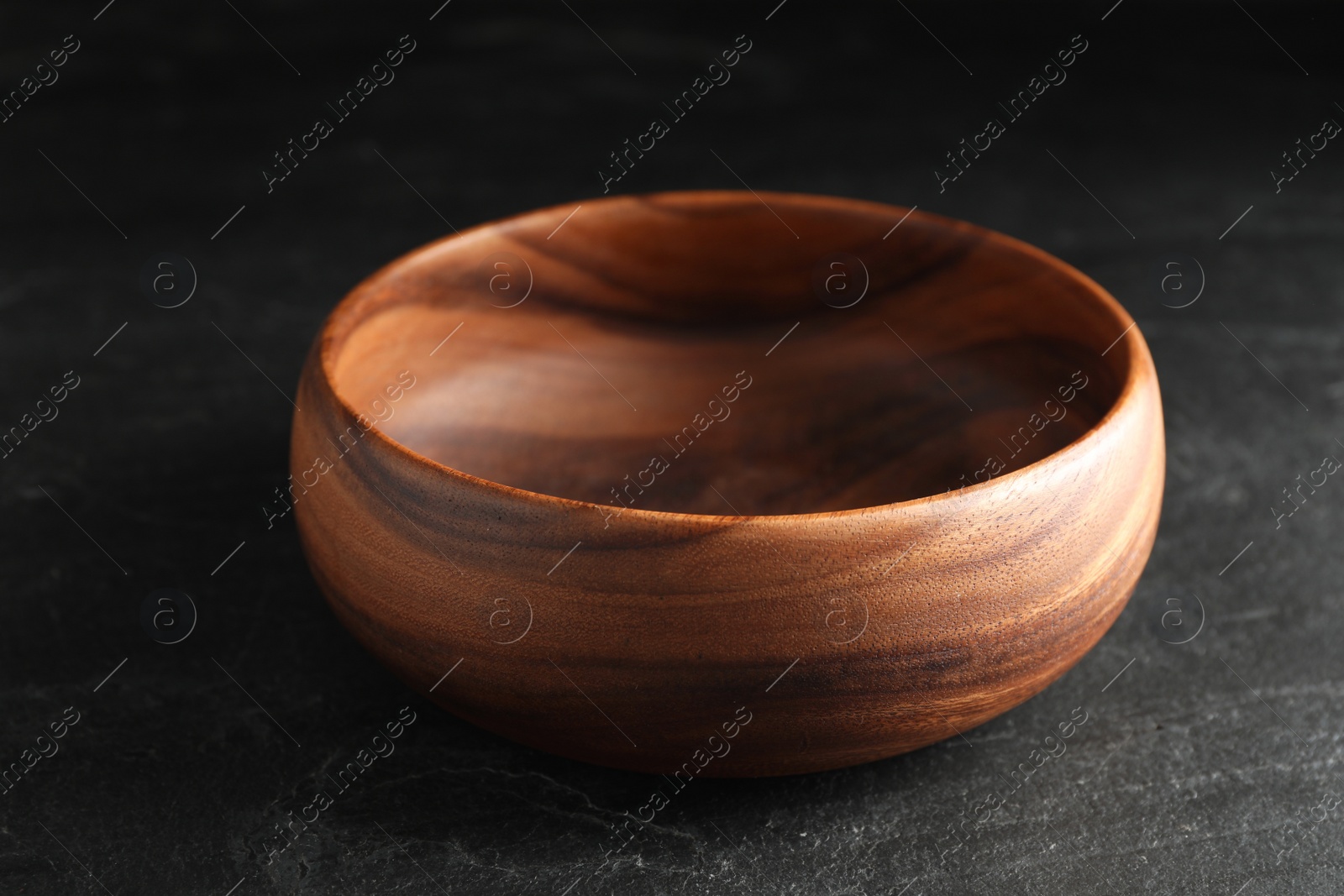 Photo of Empty clean wooden bowl on black table, closeup