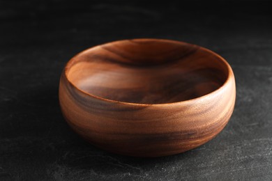 Empty clean wooden bowl on black table, closeup