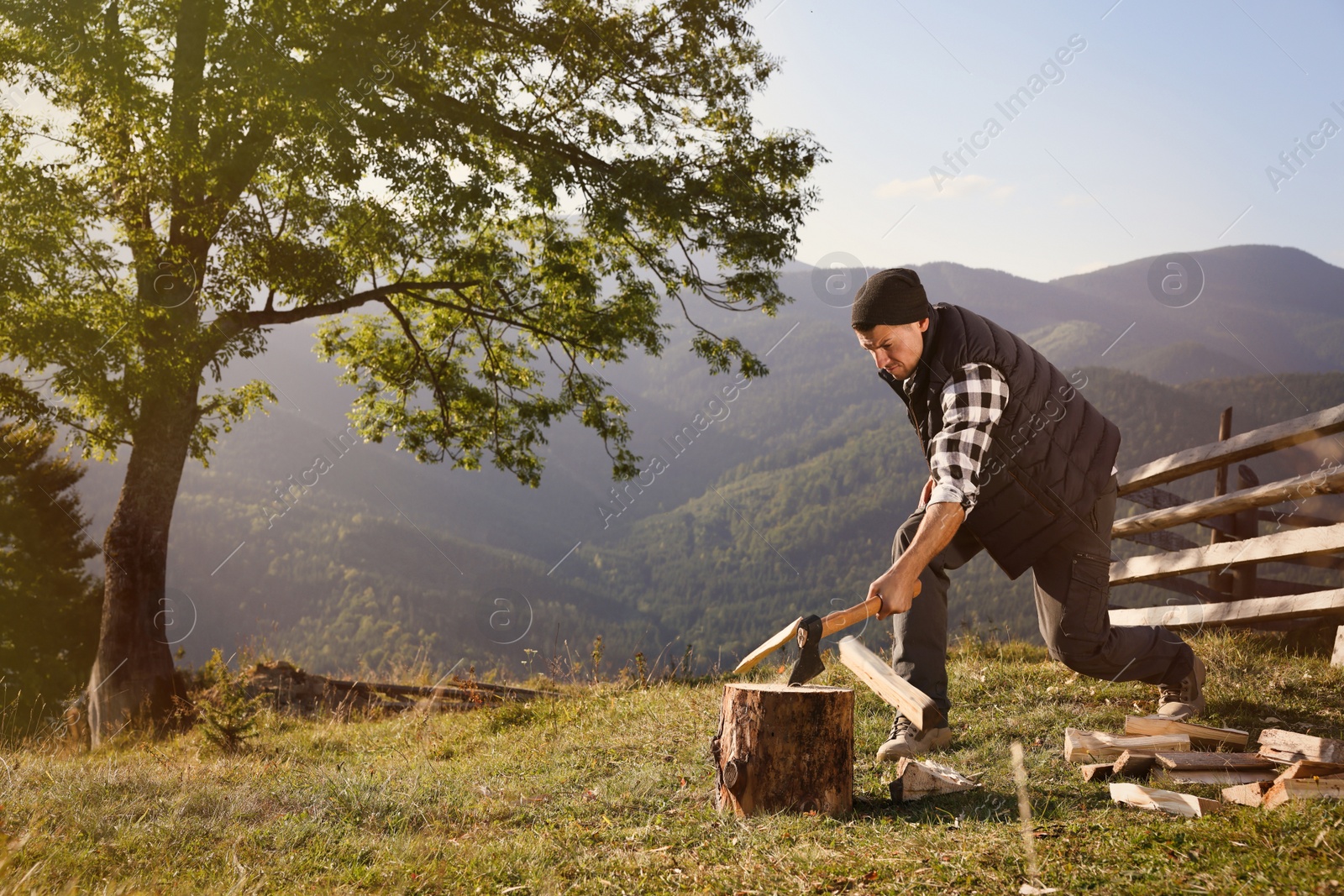 Photo of Handsome man with axe cutting firewood in mountains