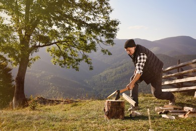 Handsome man with axe cutting firewood in mountains