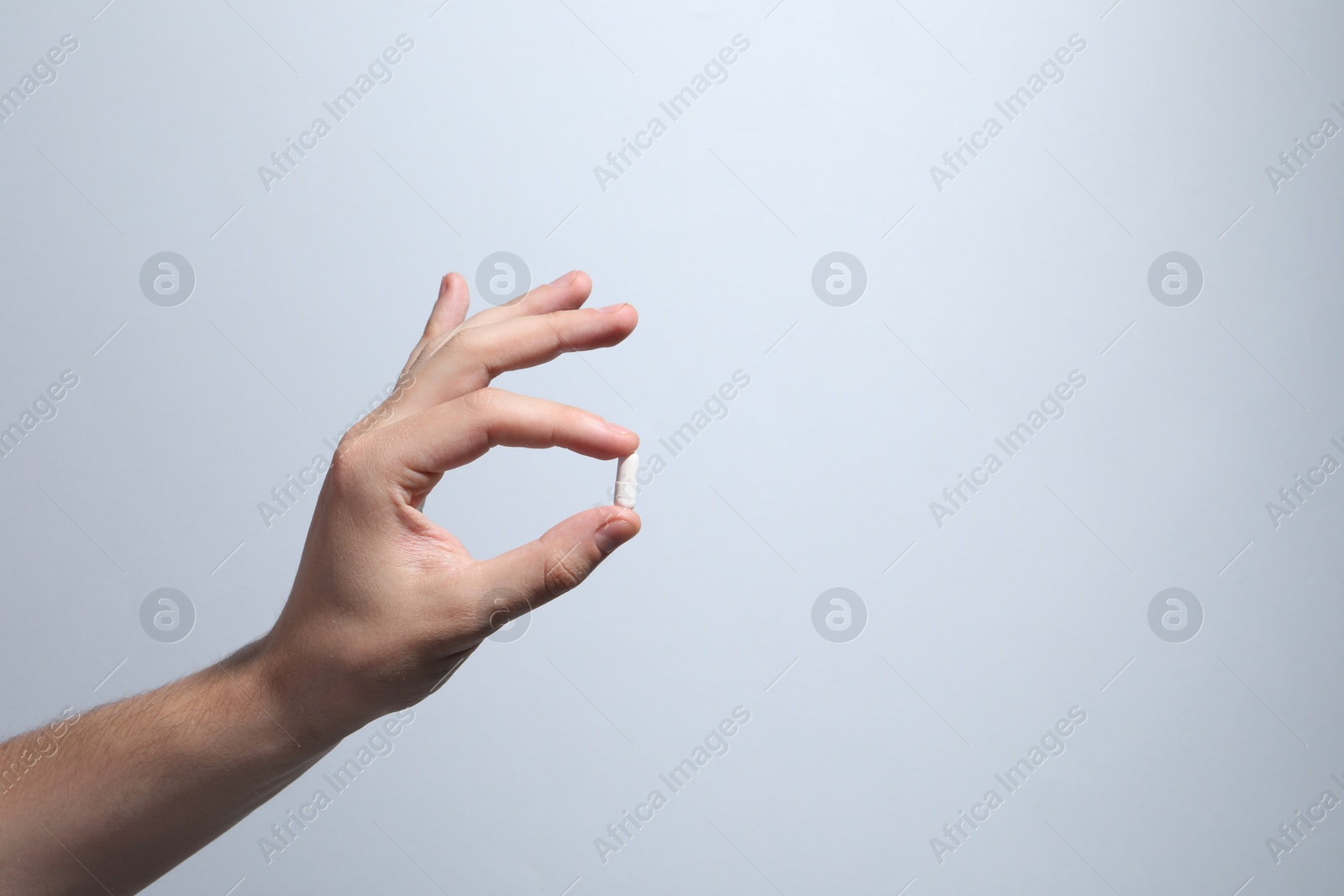 Photo of Man holding pill on light grey background, closeup. Space for text