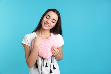 Photo of Portrait of young woman with decorative heart shaped pillow on color background, space for text
