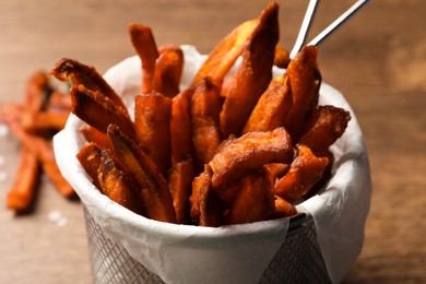 Photo of Frying basket with sweet potato fries on table, closeup
