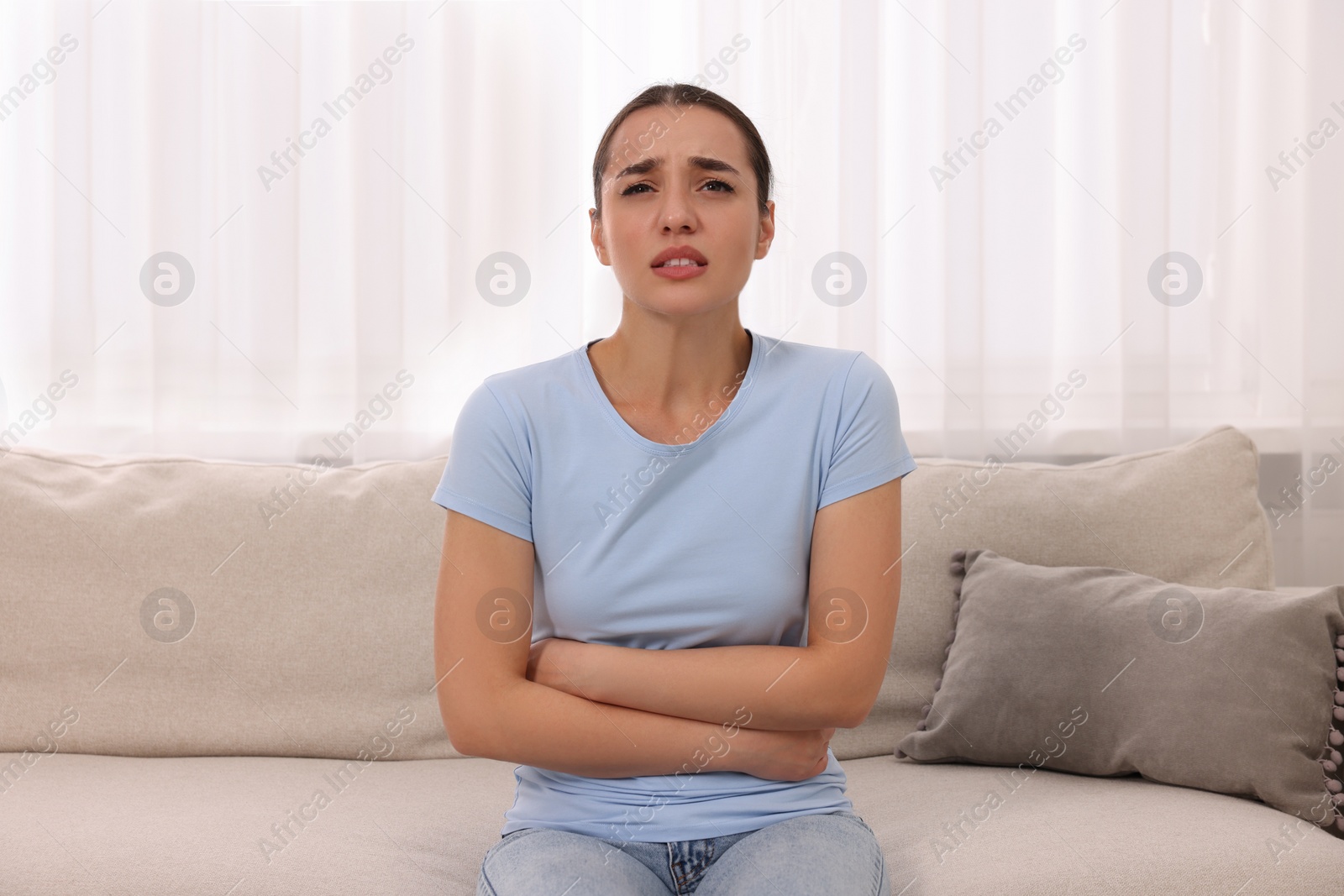 Photo of Woman suffering from abdominal pain on sofa at home. Unhealthy stomach