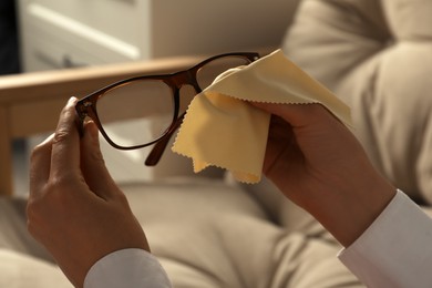 Photo of Woman cleaning glasses with cloth indoors, closeup