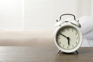 Photo of White alarm clock on wooden table in bedroom, space for text