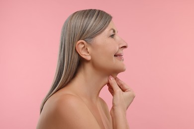 Mature woman touching her neck on pink background