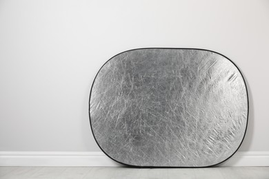 Studio reflector near grey wall in room, space for text. Professional photographer's equipment