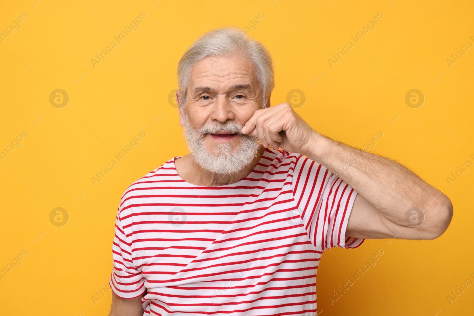 Photo of Senior man touching mustache on orange background