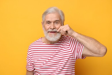 Photo of Senior man touching mustache on orange background