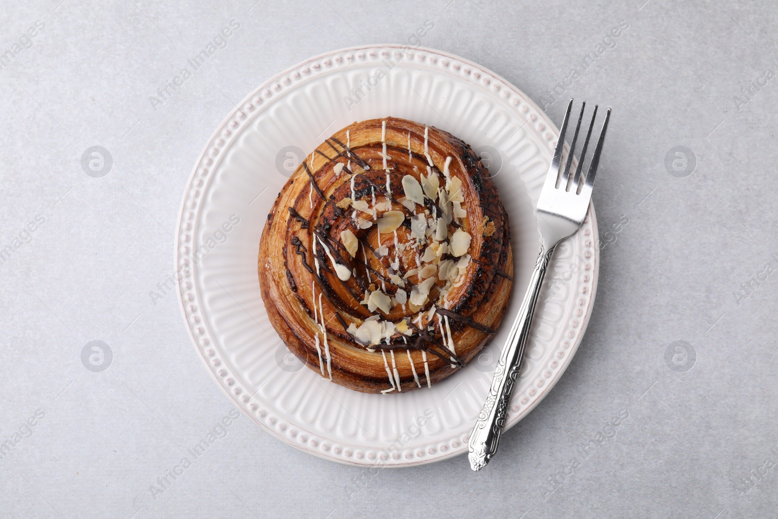 Photo of Delicious roll with poppy seeds, topping and fork served on light grey table, top view. Sweet bun