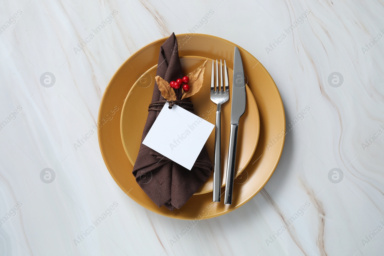 Photo of Thanksgiving table setting. Plates, cutlery, napkin, empty card and autumn decor on white marble background, top view