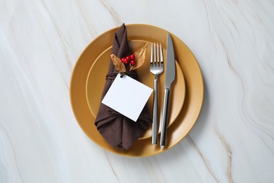 Thanksgiving table setting. Plates, cutlery, napkin, empty card and autumn decor on white marble background, top view