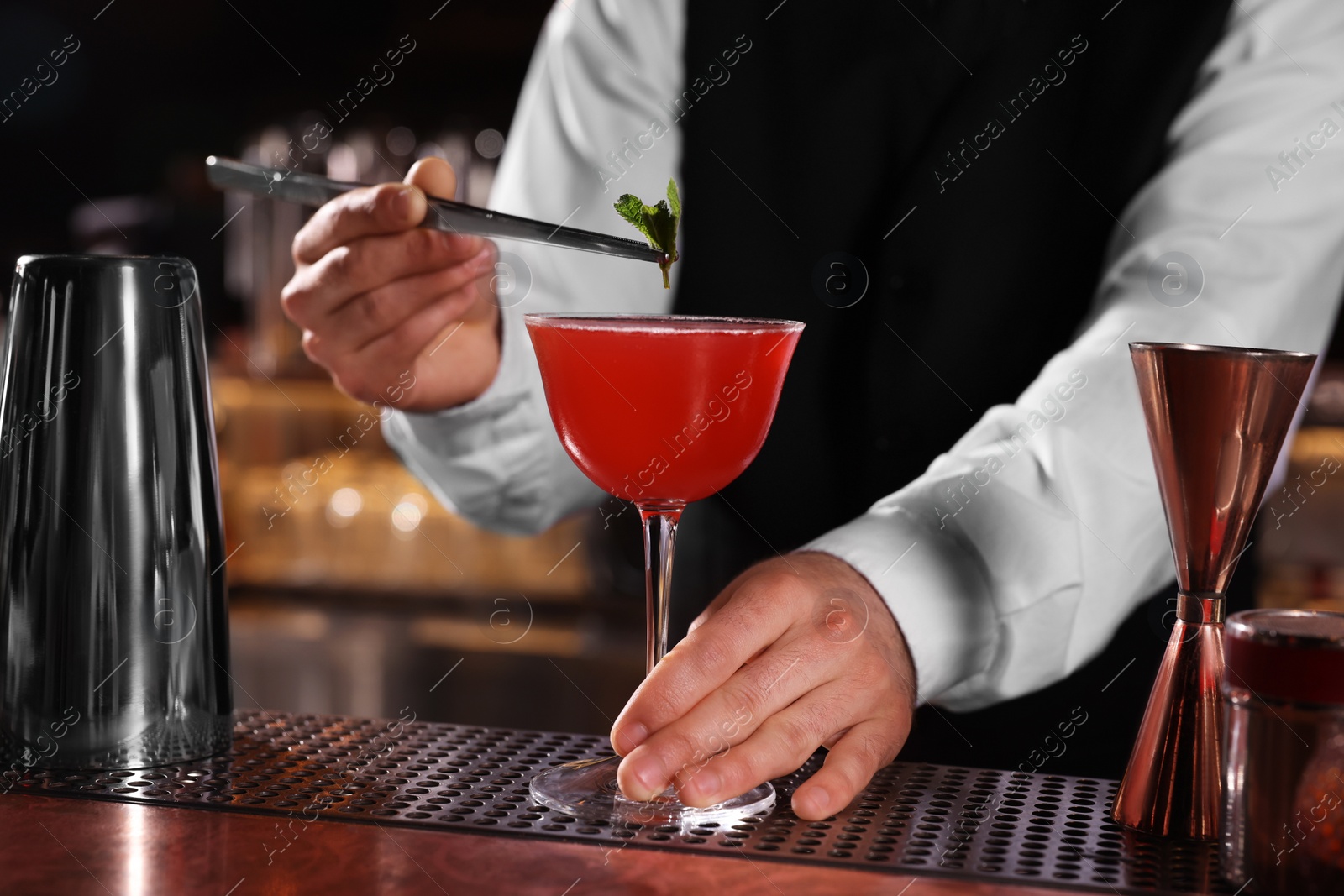 Photo of Bartender preparing fresh Martini cocktail in glass at bar counter, closeup