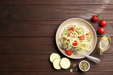 Photo of Delicious zucchini pasta with cherry tomatoes served on wooden table, flat lay. Space for text