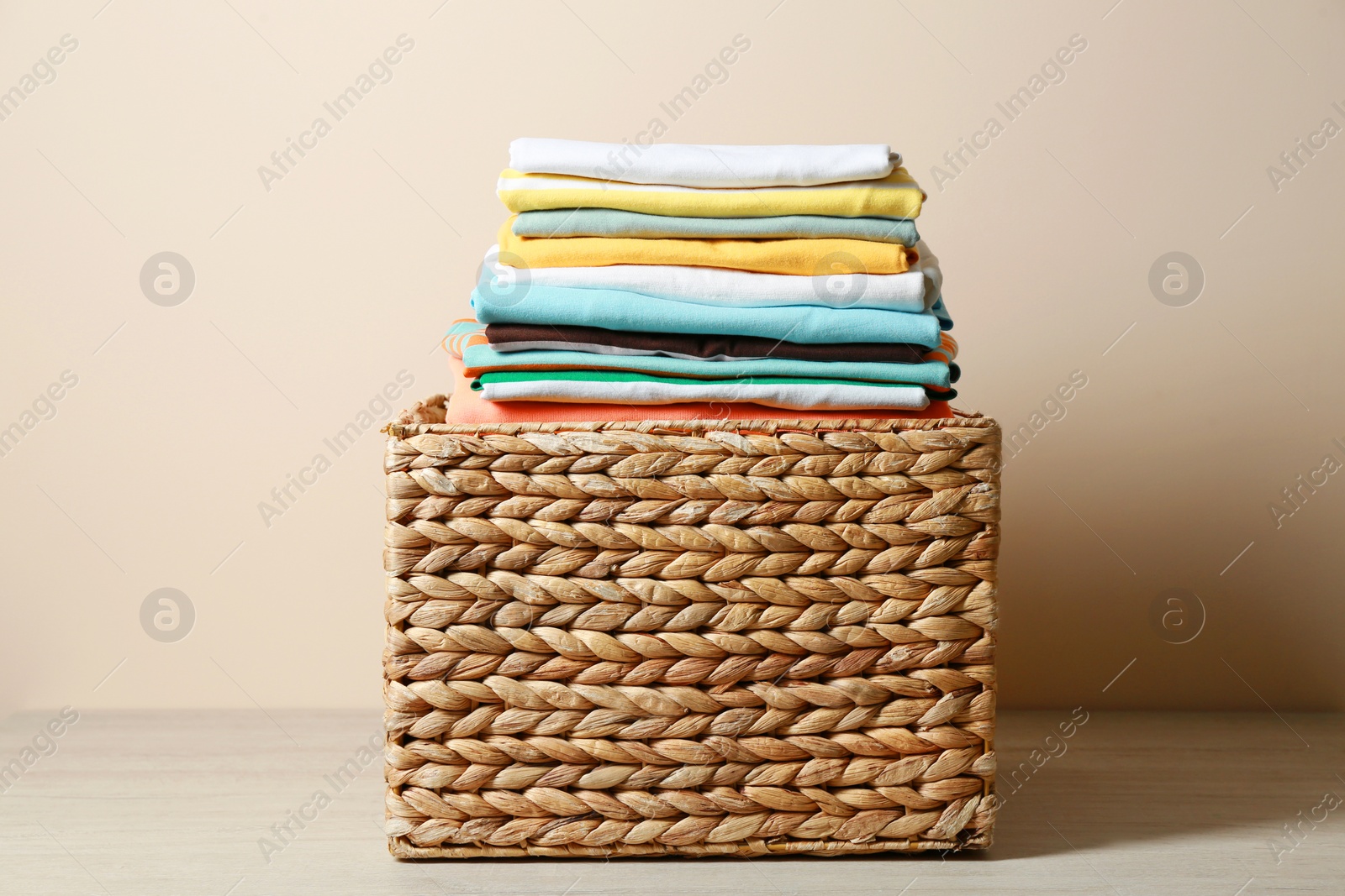 Photo of Wicker laundry basket with clean clothes on floor near beige wall