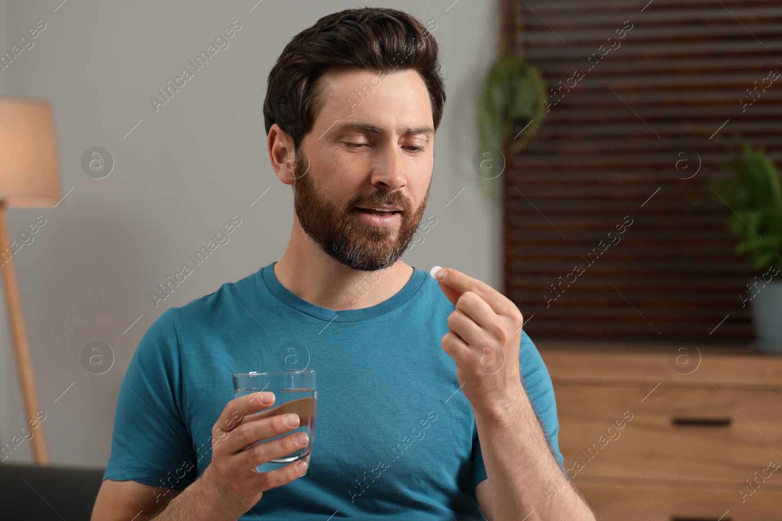 Photo of Handsome man with glass of water taking pill at home