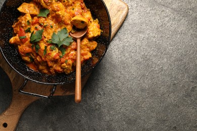 Photo of Delicious chicken curry in frying pan and spoon on grey table, top view. Space for text