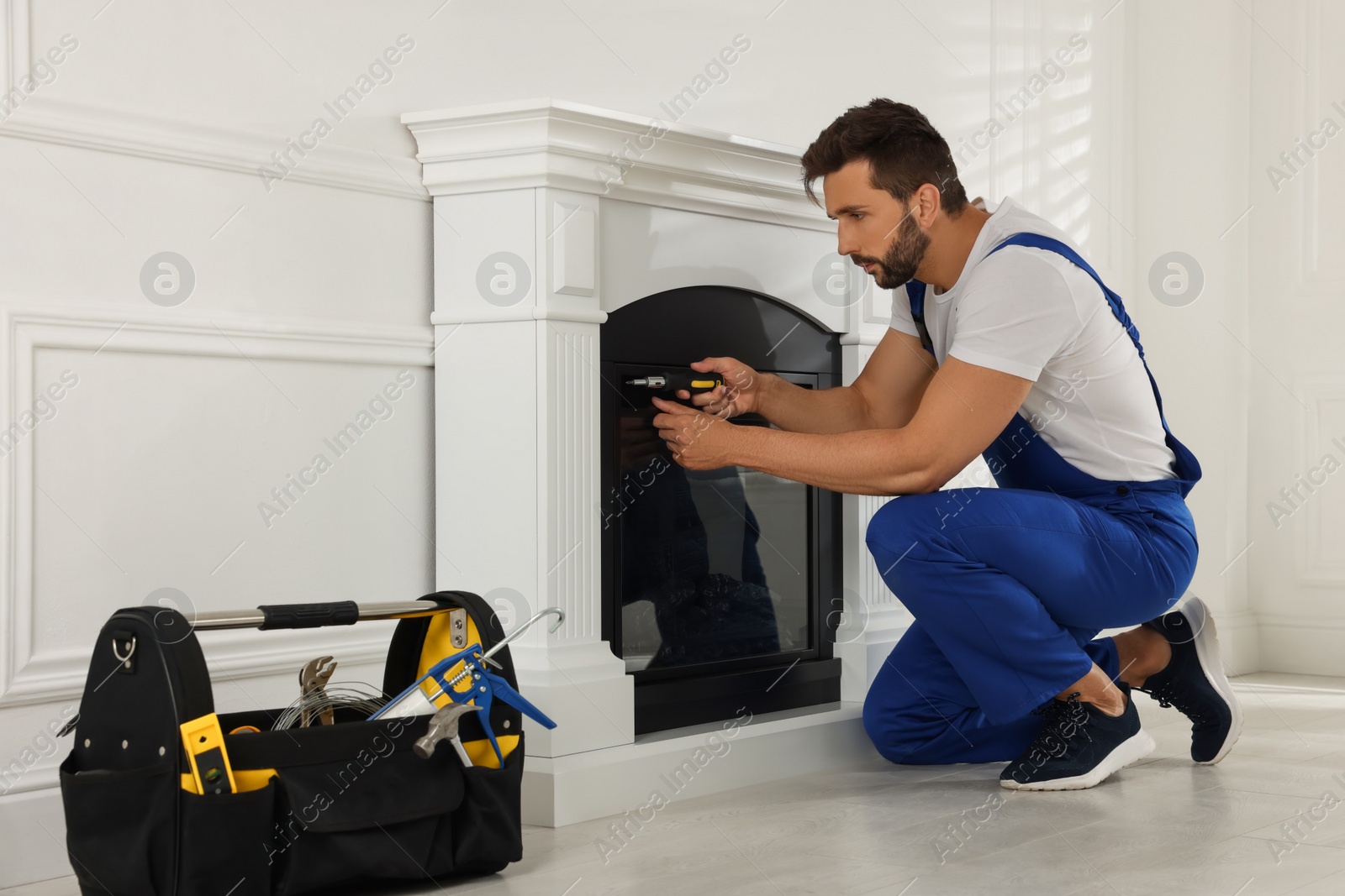 Photo of Professional technician with screwdriver installing electric fireplace in room