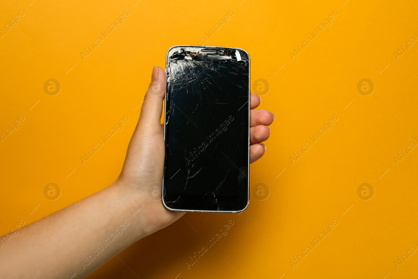 Photo of Woman holding damaged smartphone on orange background, closeup. Device repairing