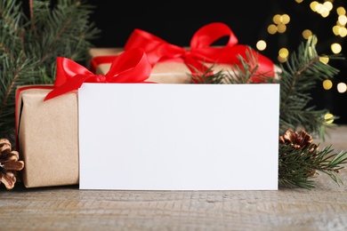 Photo of Blank greeting card near Christmas decorations and gift boxes on wooden table, closeup. Space for text