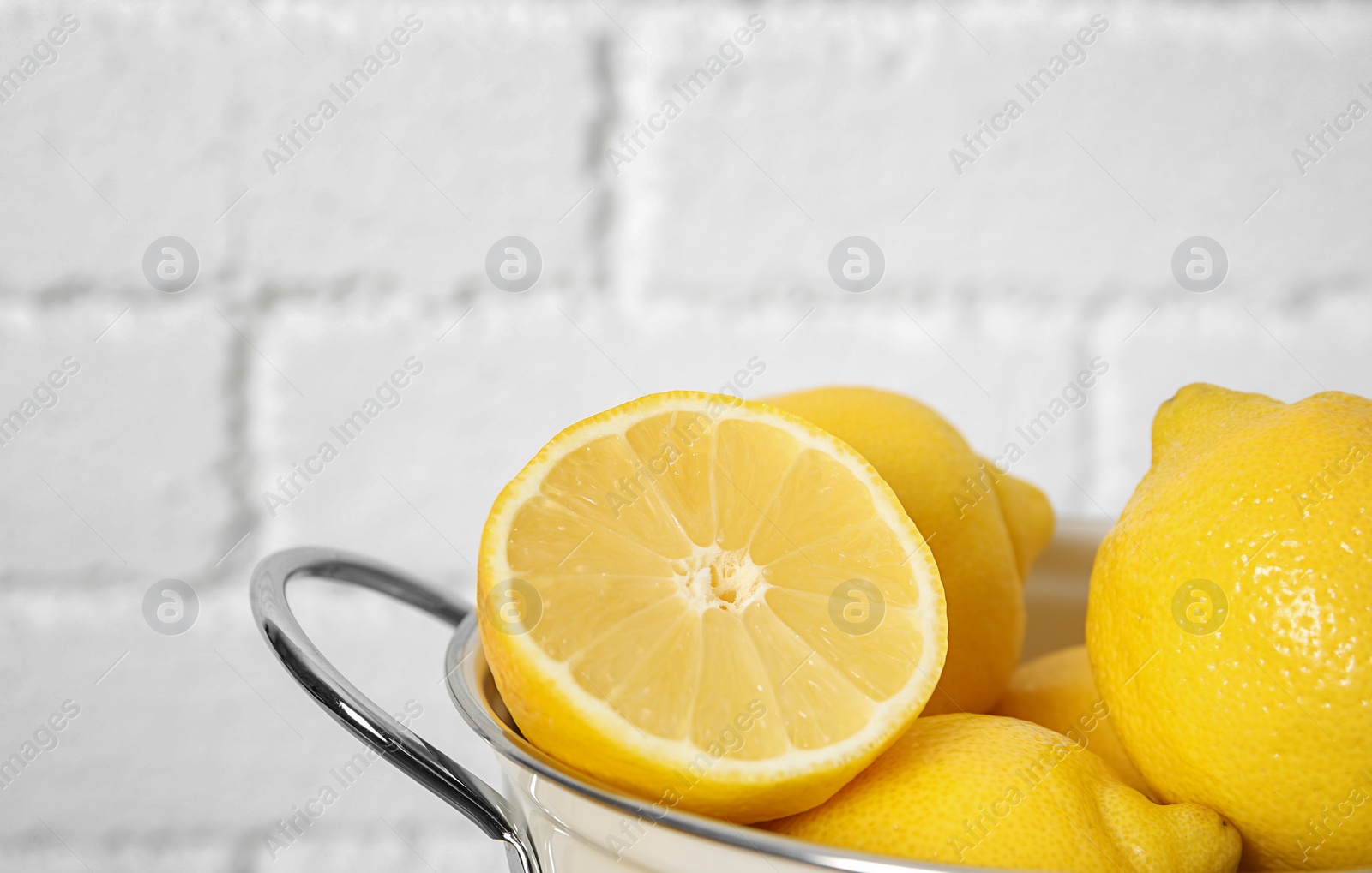 Photo of Colander with ripe lemons against brick wall