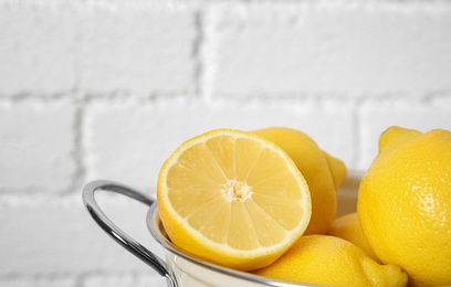 Colander with ripe lemons against brick wall