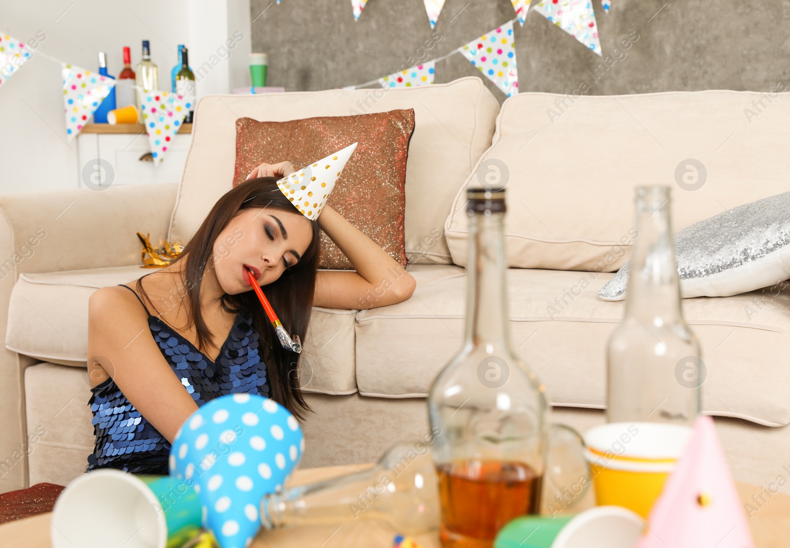 Photo of Young woman sleeping near sofa in messy room after party