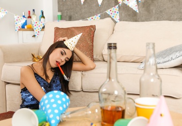 Young woman sleeping near sofa in messy room after party