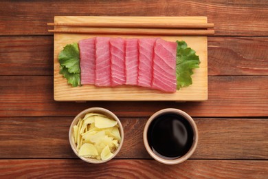 Photo of Tasty sashimi (pieces of fresh raw tuna), lettuce, soy sauce and ginger slices on wooden table, flat lay